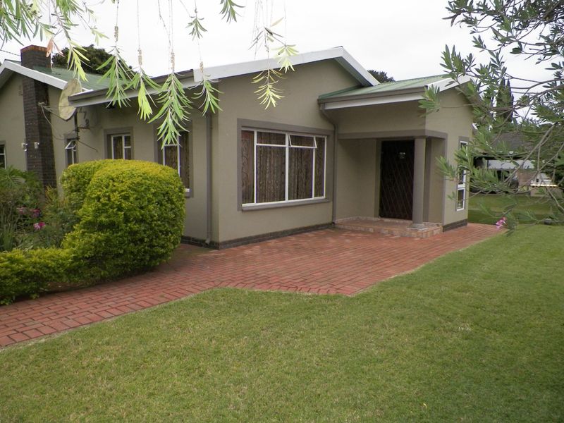 Front view of a well-maintained single-story house featuring a brick paved entrance, covered porch, and established garden.