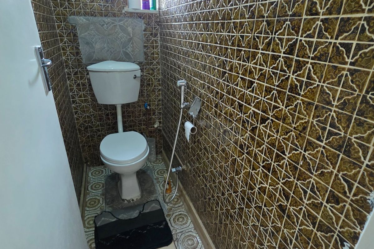 A compact guest toilet featuring vintage patterned wall and floor tiles, equipped with a standard white toilet suite and bidet spray.