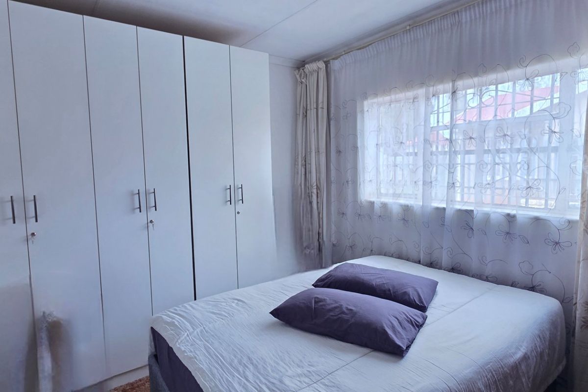 A functional bedroom featuring built-in white cabinetry and a window with security bars, providing essential storage and natural light.
