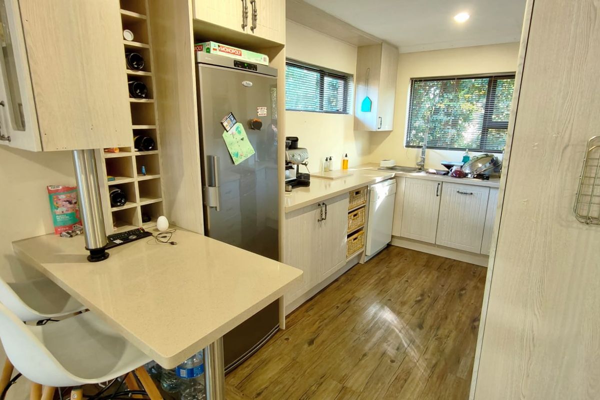 A functional kitchen featuring light wood-grain cabinetry, stone countertops, a built-in wine rack, and durable laminate flooring with ample natural light.