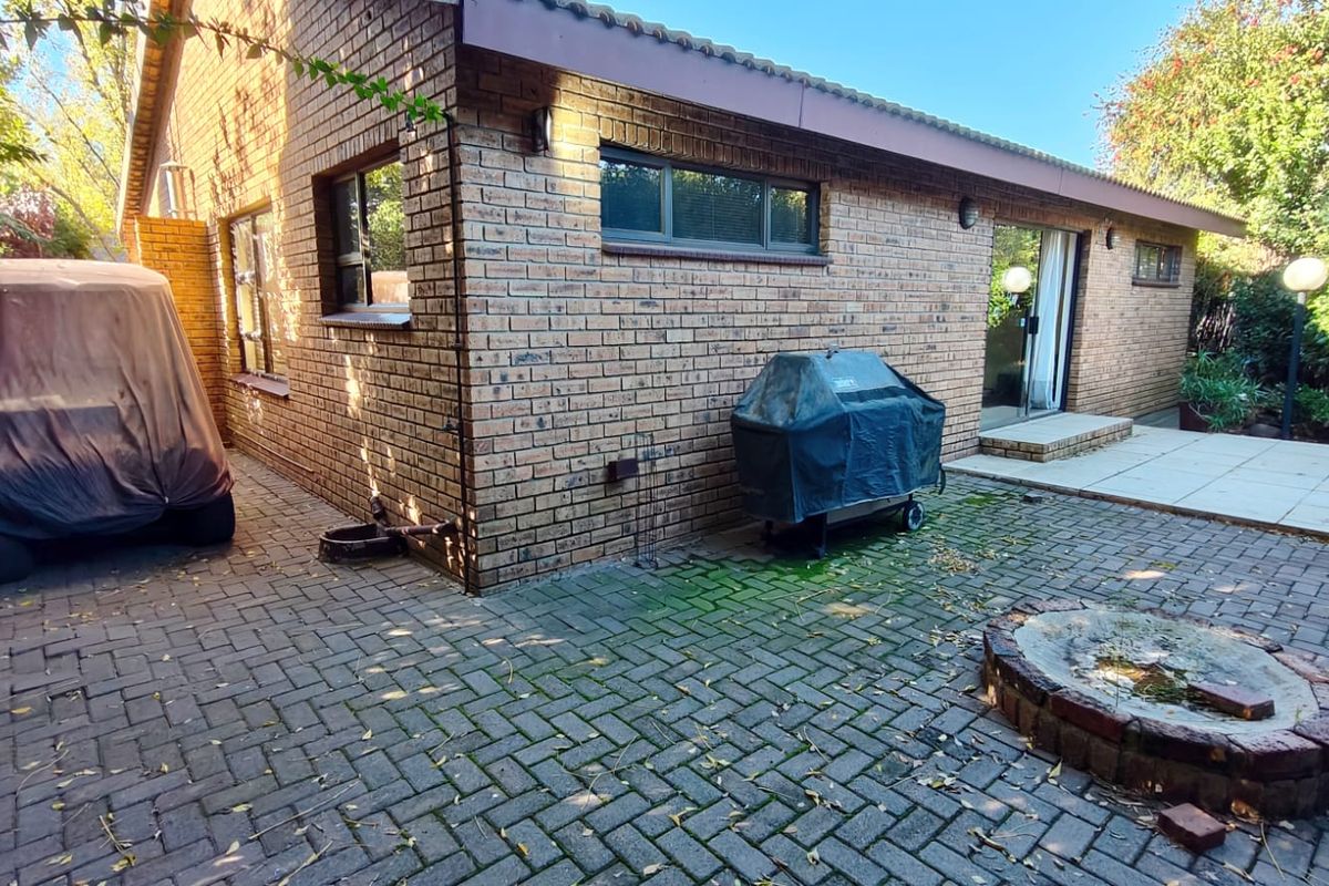 Rear exterior view of a brick house featuring a paved patio area, sliding glass door access, and a built-in brick fire pit.