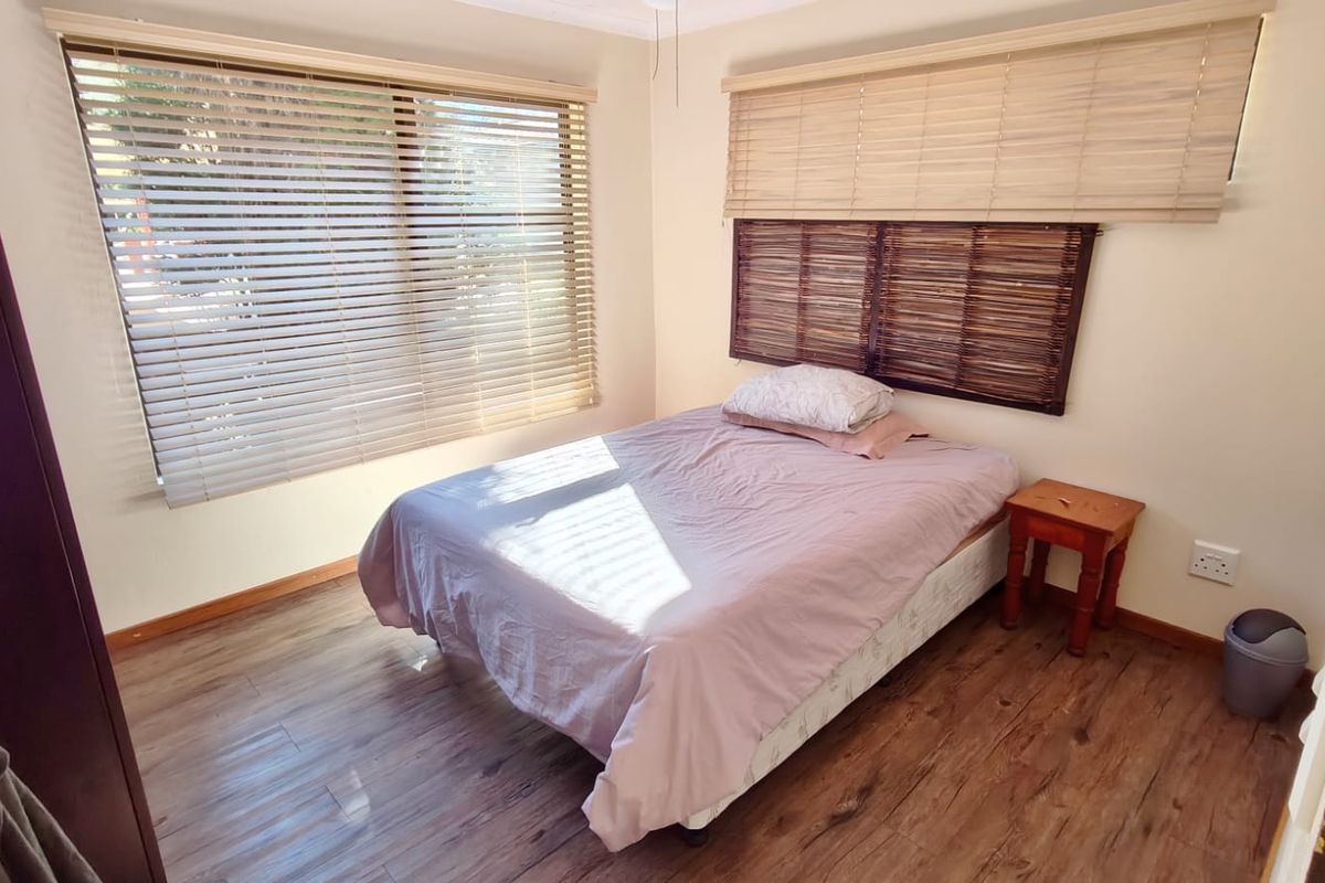 A bedroom featuring laminate flooring and dual-style window blinds, providing a functional space with natural light.