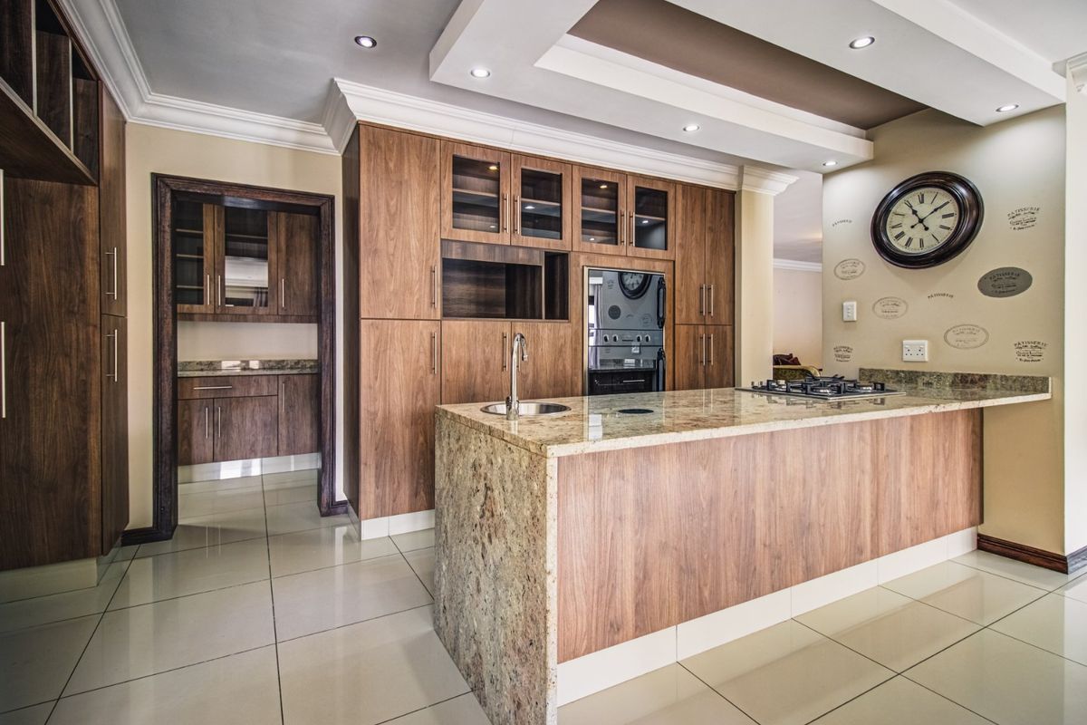 Modern kitchen featuring high-quality wooden cabinetry, granite countertops, a central island with a gas hob, and integrated appliances with recessed ceiling lighting.