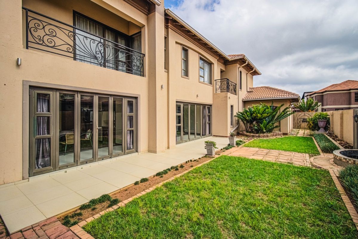 Rear view of a double-storey residence featuring a tiled patio, aluminium stacker doors, wrought iron balcony railings, and a well-maintained garden.