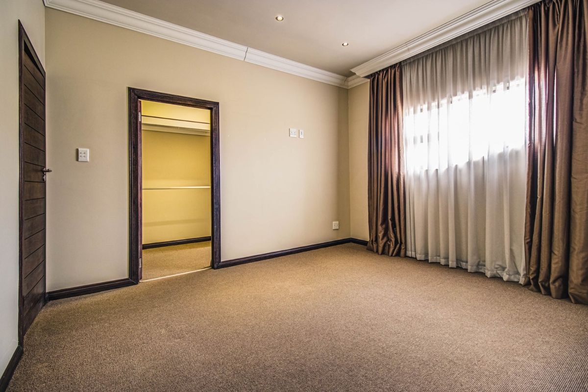 A spacious, neutral-toned bedroom featuring plush carpeting, crown molding, recessed lighting, and an integrated walk-in closet.