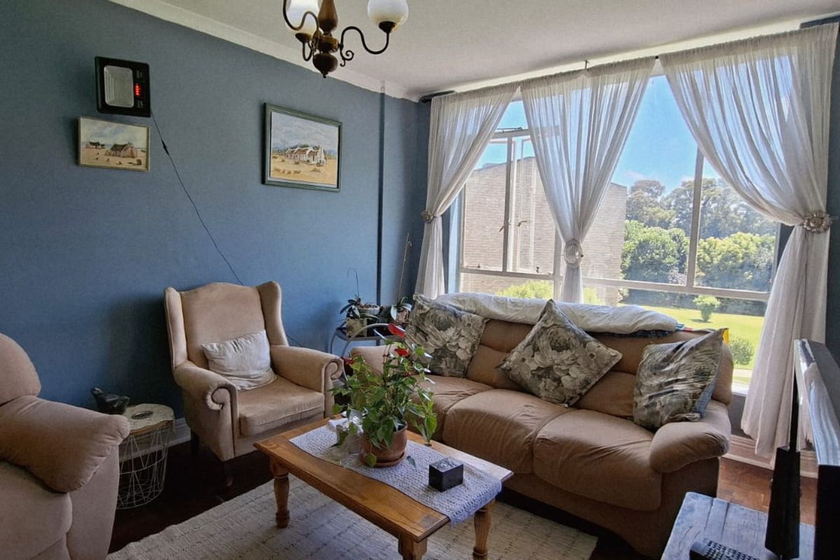 A comfortable living room featuring parquet flooring, a large window providing natural light, and blue-toned walls.