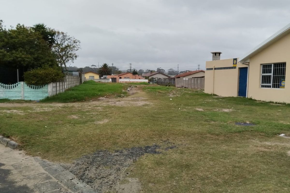 A vacant residential plot featuring a grass lawn, boundary walls, and adjacent residential structure.