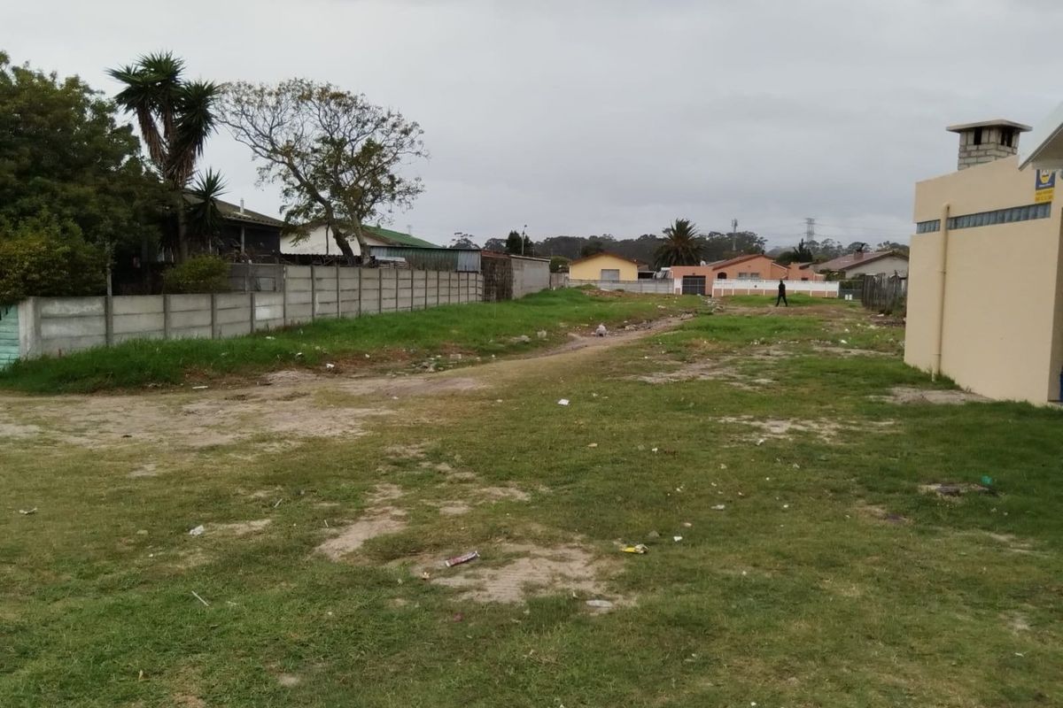 A vacant residential plot featuring a grass lawn, precast concrete boundary walls, and an adjacent structure with an external chimney.