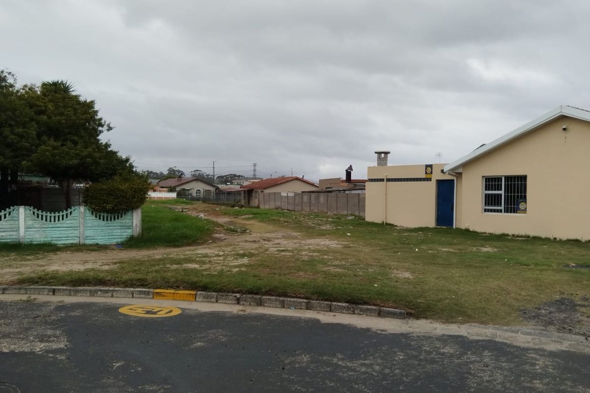 A view of a residential property exterior showing a vacant yard area, boundary wall, and the side facade of the dwelling.