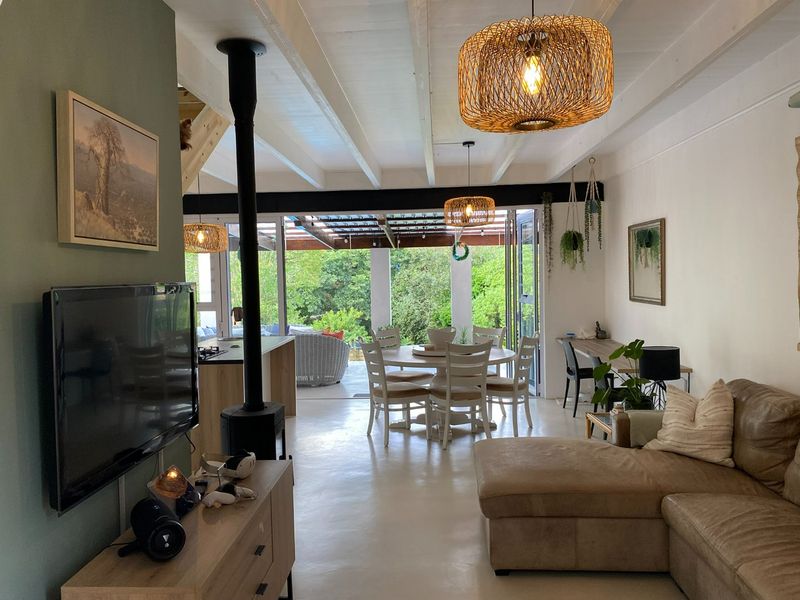 Spacious open-plan living and dining area featuring polished concrete floors, exposed beam ceilings, a modern fireplace, and seamless flow to the outdoor patio.