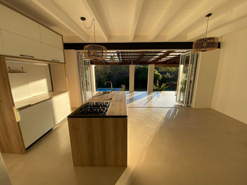 Modern open-plan kitchen featuring a central island with gas cooktop, sleek cabinetry, and seamless flow through bi-fold doors to a covered outdoor patio area.