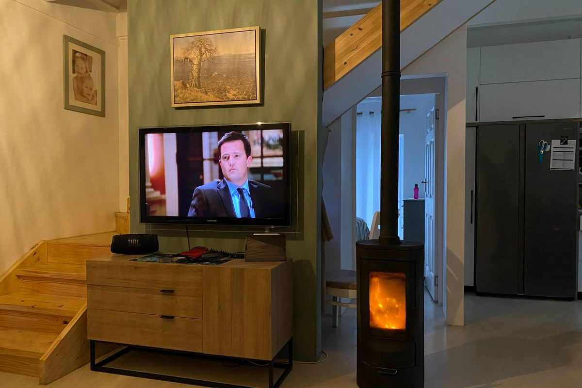 A cozy living area featuring a modern freestanding fireplace, wooden staircase, and a feature wall with integrated television setup.