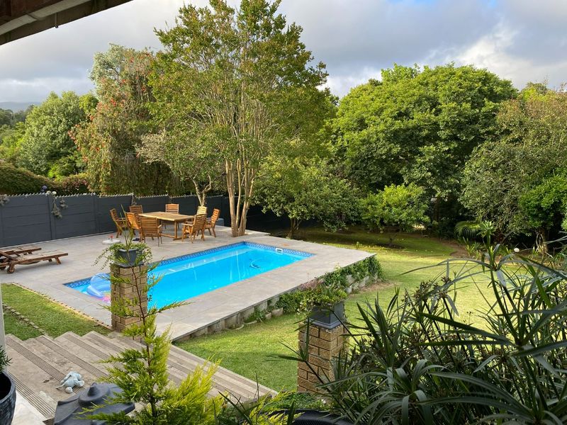 Outdoor pool area featuring a tiled deck, brick pillars, and a well-maintained garden setting, ideal for relaxation and outdoor entertainment.