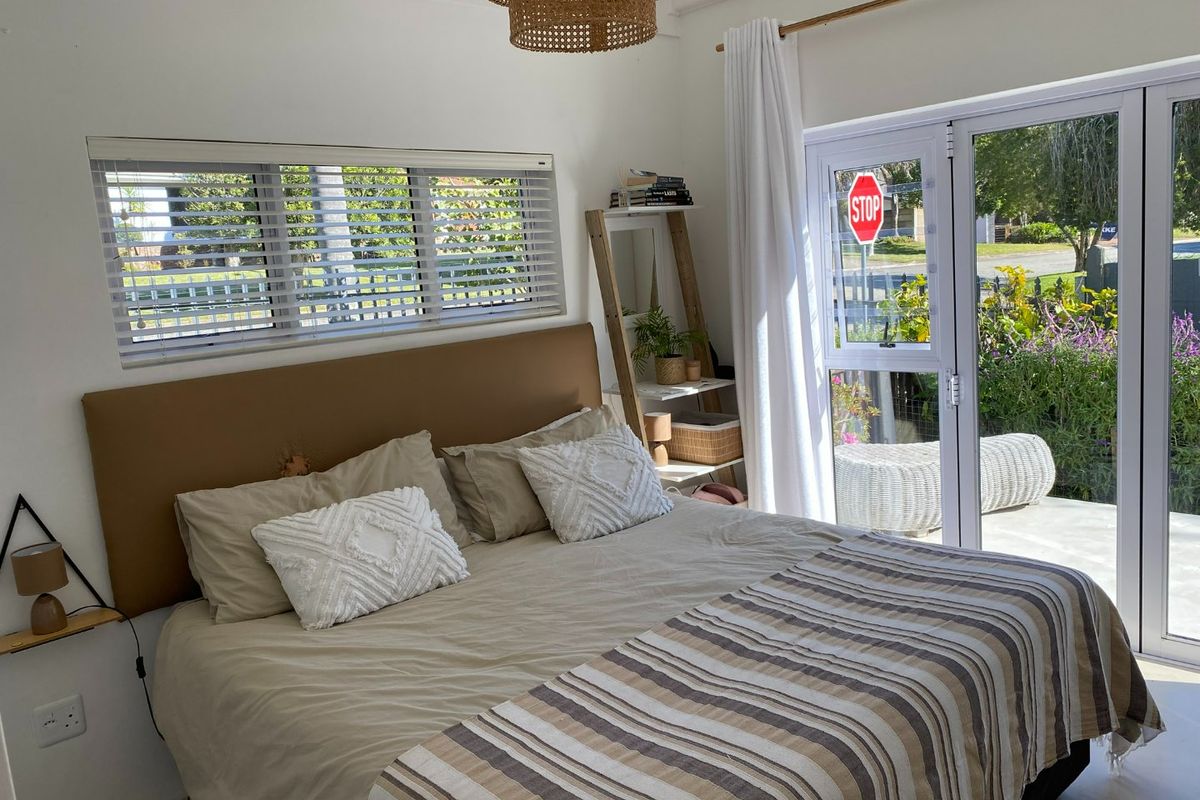 A bright bedroom featuring a large window with venetian blinds and glass french doors providing direct access to the outdoor patio area.