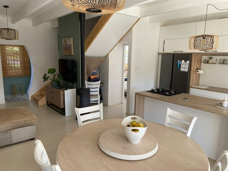 Modern open-plan living and kitchen area featuring exposed ceiling beams, a central fireplace, and a functional kitchen island with a gas hob.