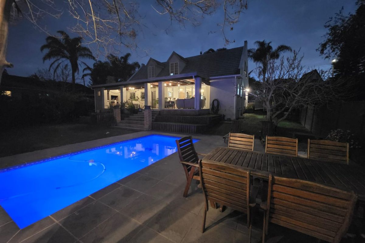 Night view of the rear exterior featuring a swimming pool, paved patio area, and a covered veranda attached to the main house structure.
