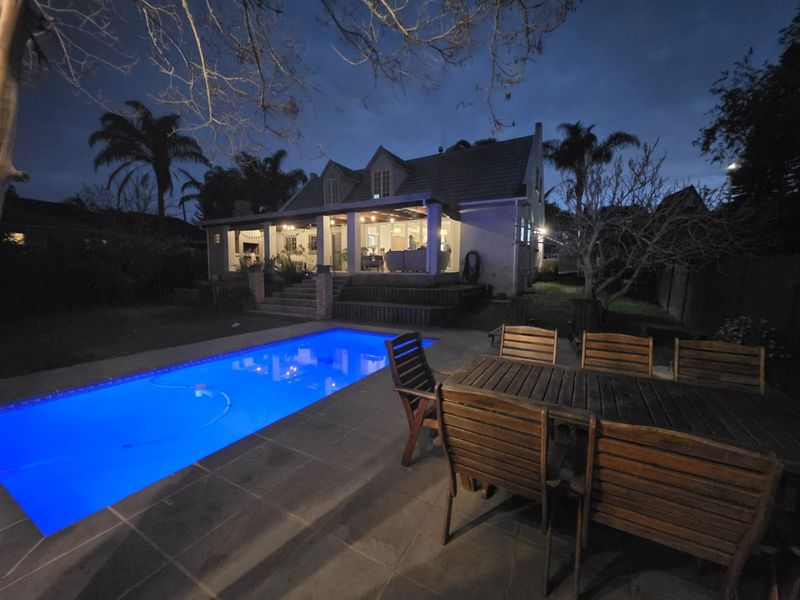 Night view of the rear exterior featuring a swimming pool, paved patio area, and a covered veranda attached to the main house structure.