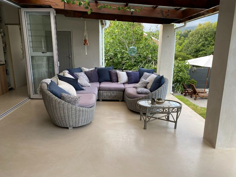 A covered outdoor patio featuring a timber pergola, smooth concrete flooring, and seamless access to the interior through large sliding glass doors.