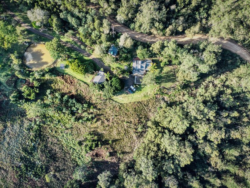 Aerial view of a rural farm property featuring multiple buildings, a dam, solar infrastructure, and extensive surrounding woodland.