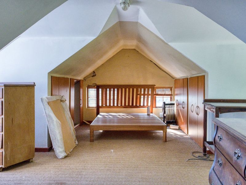 Attic-style bedroom featuring sloped ceilings, built-in wooden cupboards, and carpeted flooring, offering a cozy layout with potential for modernization.