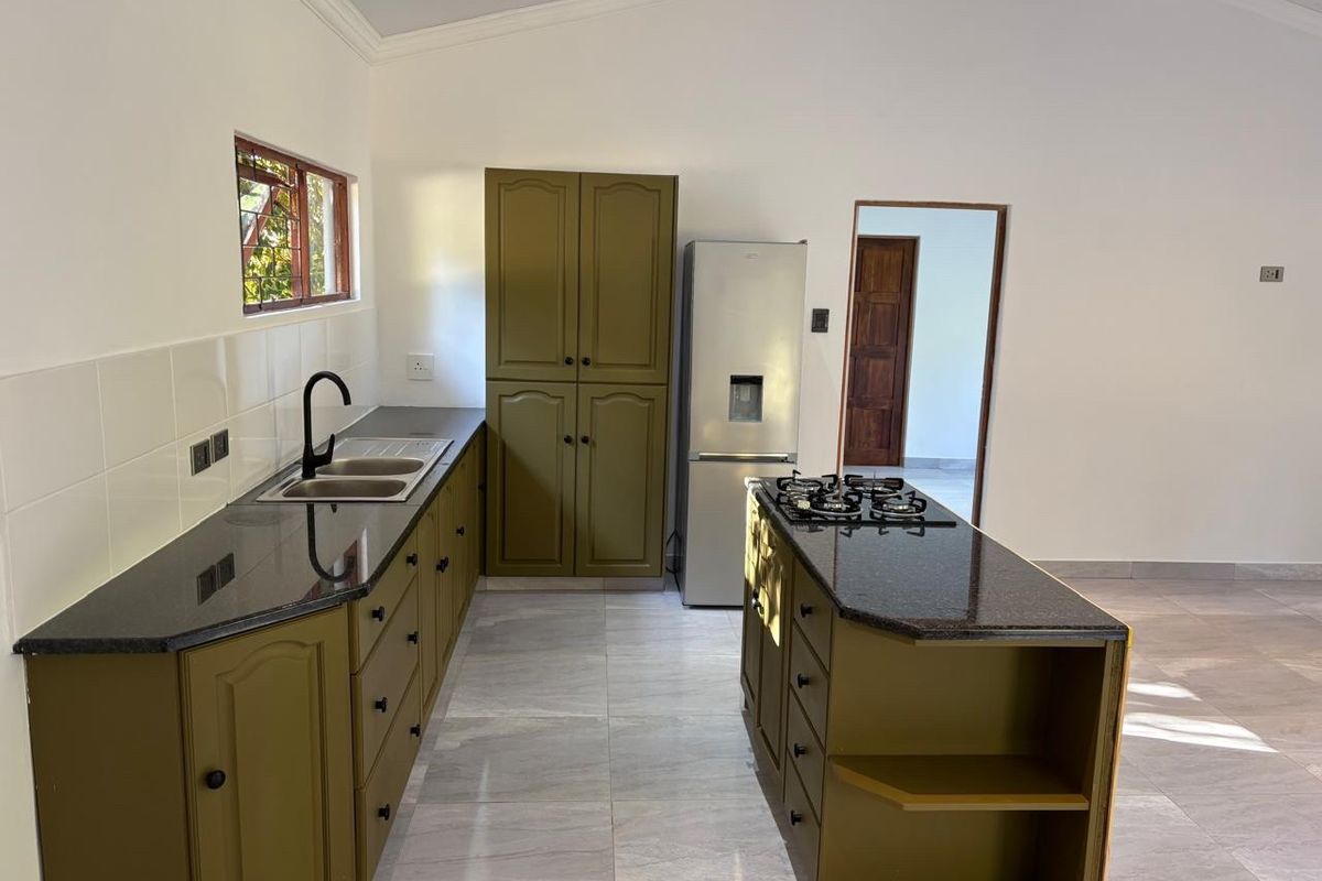 A clean, modern kitchen featuring olive-toned cabinetry, granite countertops, a central island with a gas hob, and tiled flooring throughout.