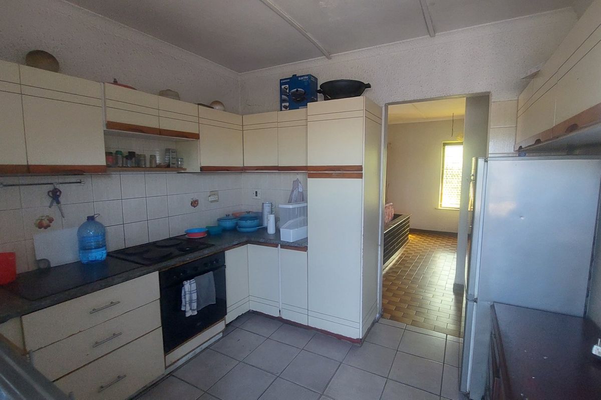A functional kitchen featuring built-in cabinetry, an electric hob, and an oven, with tiled splashbacks and flooring, offering potential for modernization.