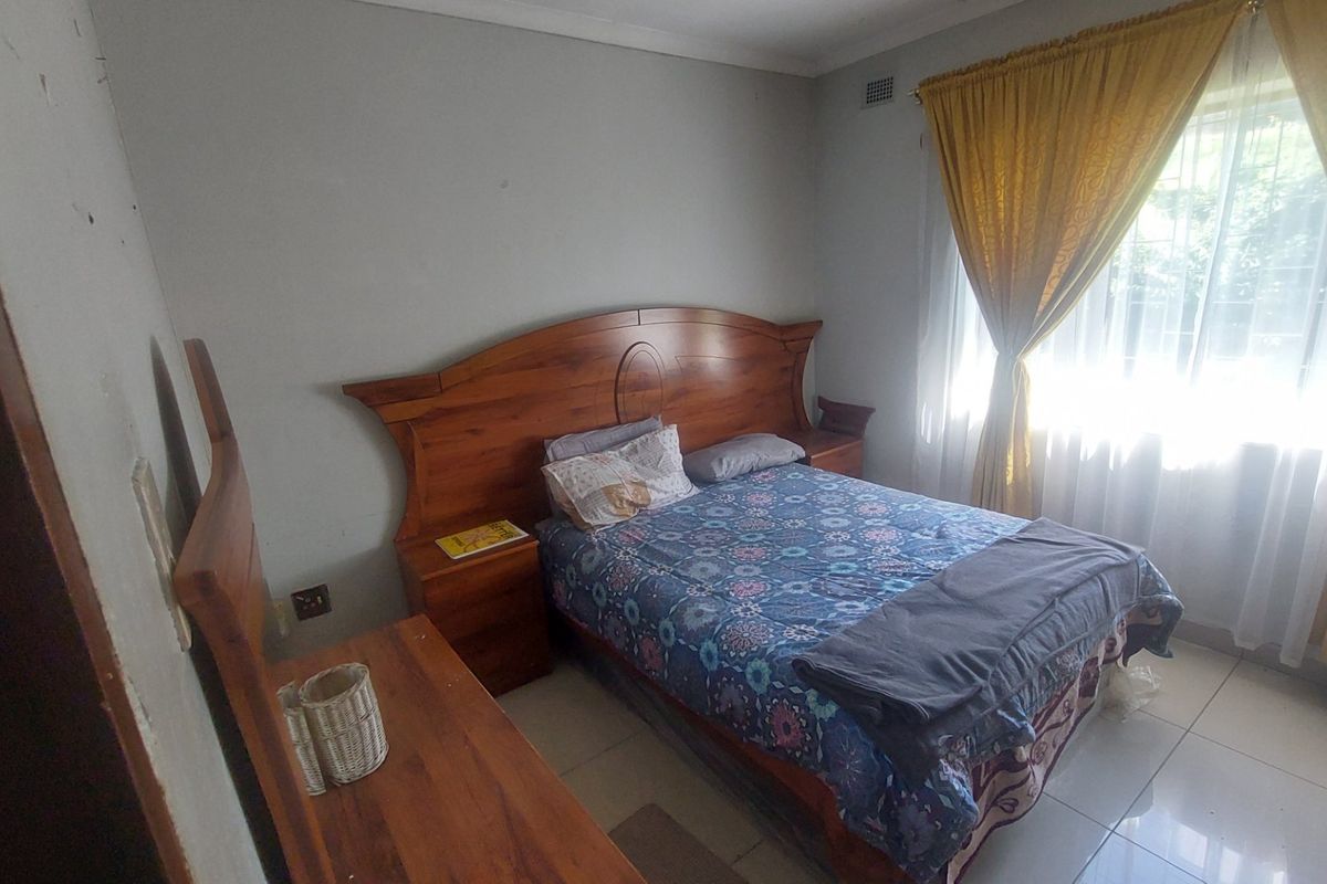 A standard bedroom featuring tiled flooring and natural light through a window with curtain rails.