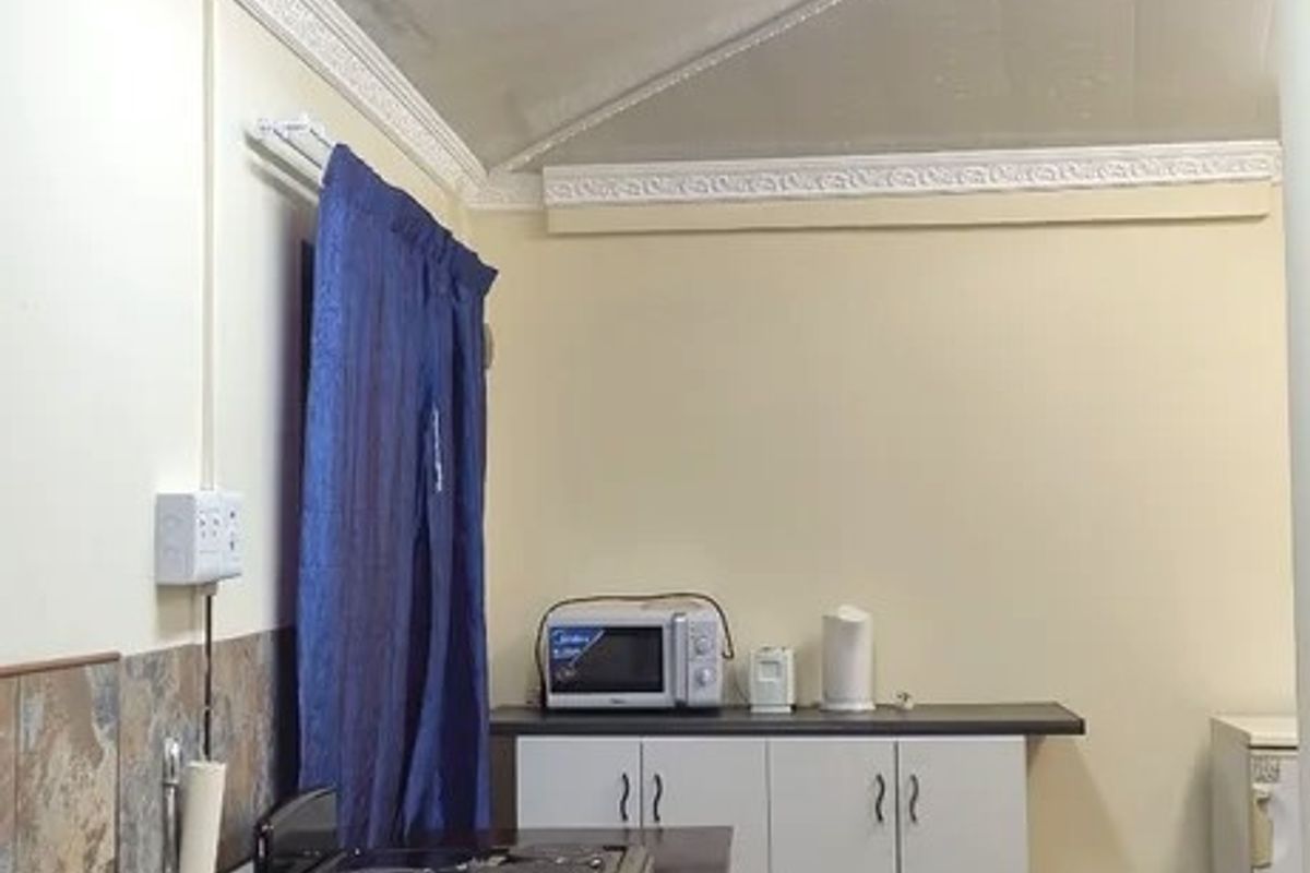 A compact kitchen area featuring a stainless steel sink, built-in cabinetry, and a freestanding stove, with a sloped ceiling and carpeted flooring.
