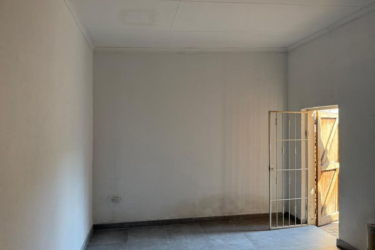 An empty, neutral-toned room featuring tiled flooring and a security gate leading to an exterior entrance.
