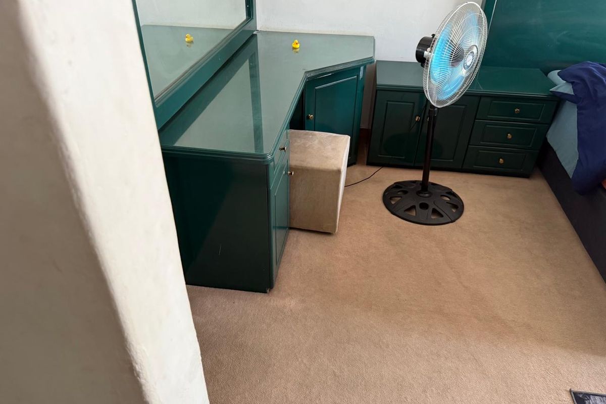 A bedroom featuring built-in green cabinetry and vanity unit with integrated mirror, finished with carpeted flooring.