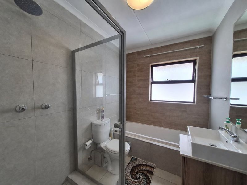Modern bathroom featuring a walk-in shower with glass enclosure, a built-in bathtub, and a contemporary vanity basin with neutral wall tiling.
