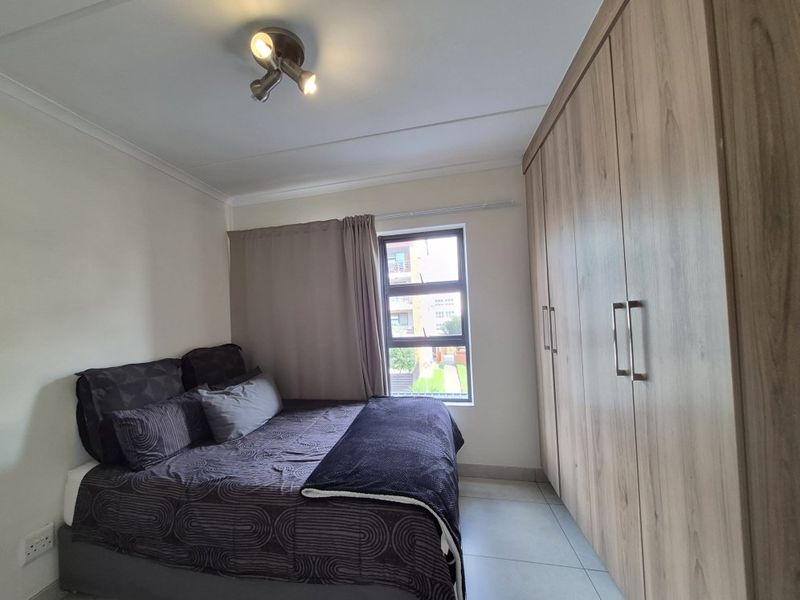 A well-maintained bedroom featuring neutral tiled flooring, ample built-in wooden cupboards, and a modern ceiling spotlight fixture.