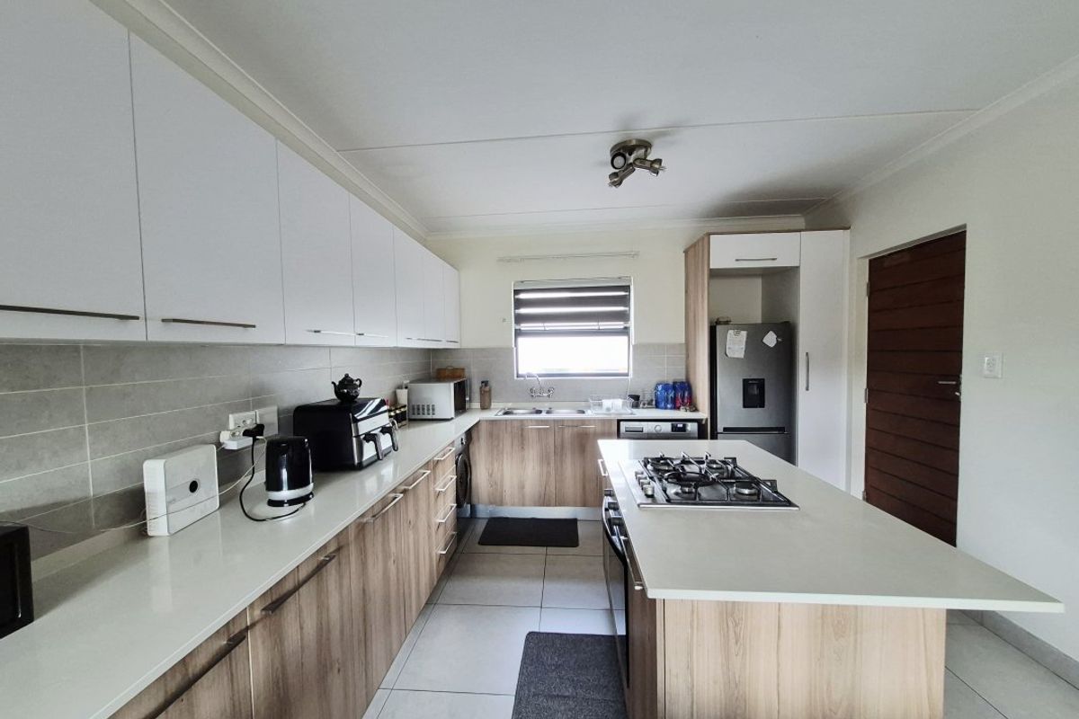 Modern kitchen featuring wood-finish cabinetry, stone countertops, a central island with a gas hob, and tiled flooring throughout.