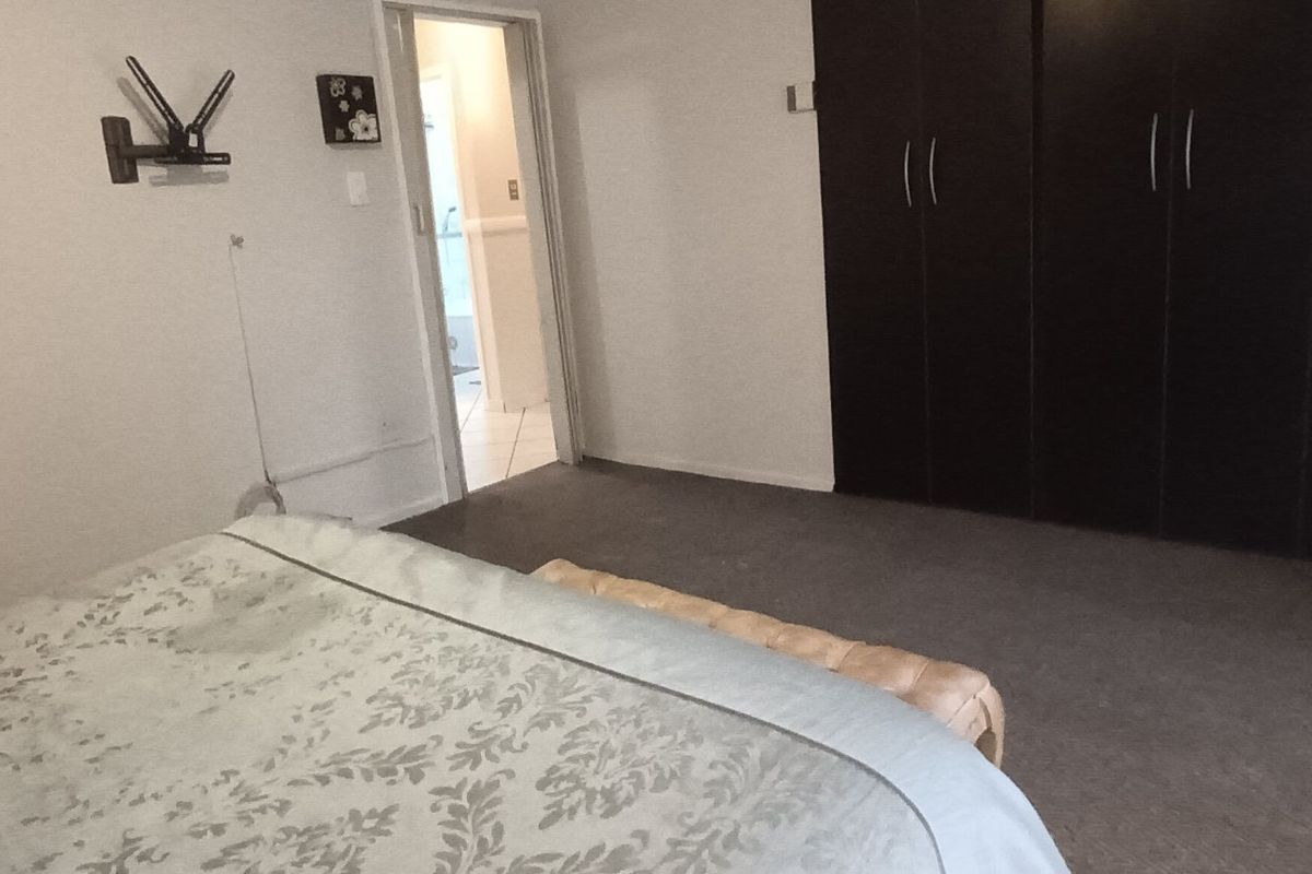 A bedroom featuring built-in dark wood cabinetry and carpeted flooring, with an adjacent doorway leading to an en-suite bathroom.
