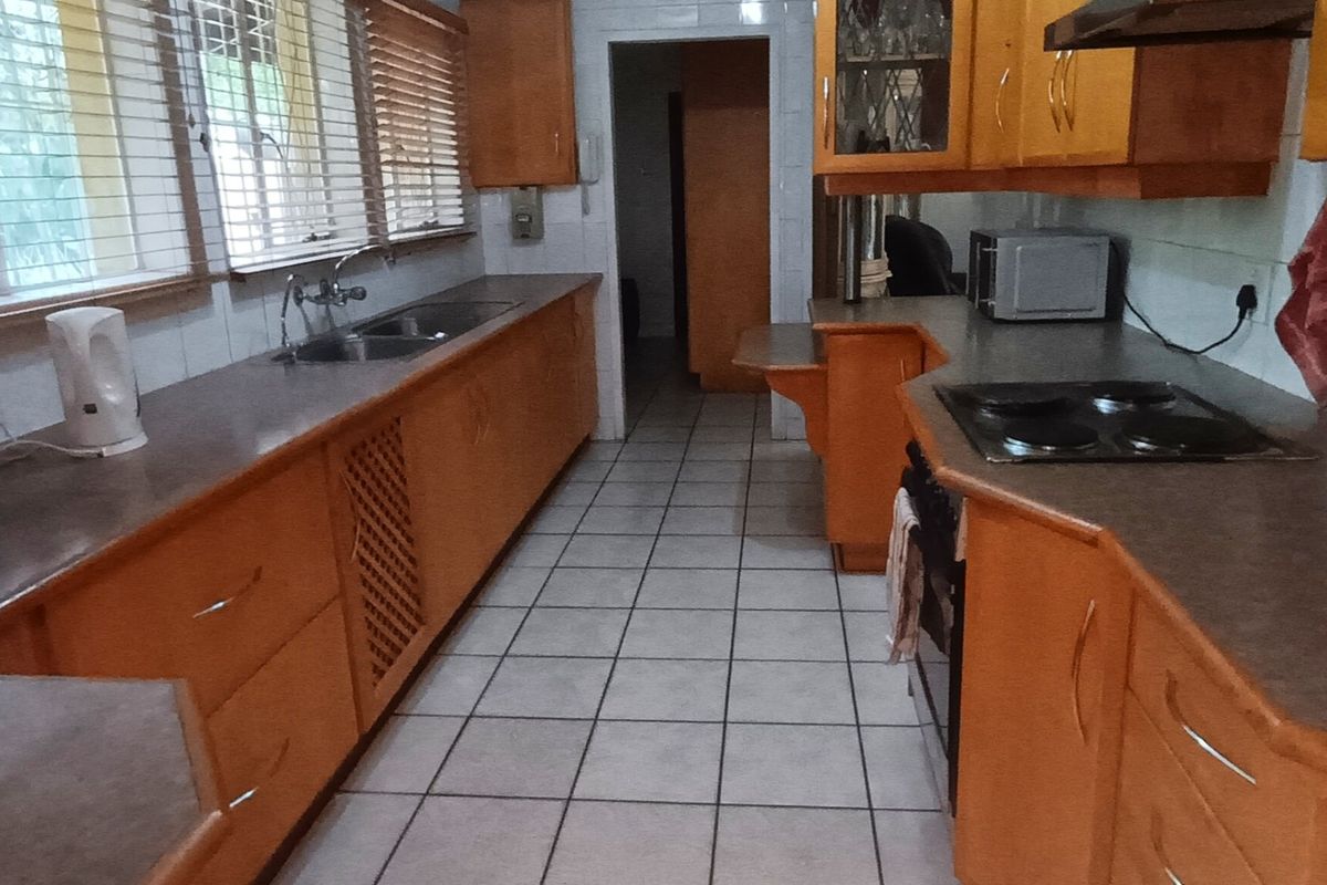 A functional kitchen featuring wooden cabinetry, laminate countertops, a built-in electric hob, and tiled flooring with a double sink setup.