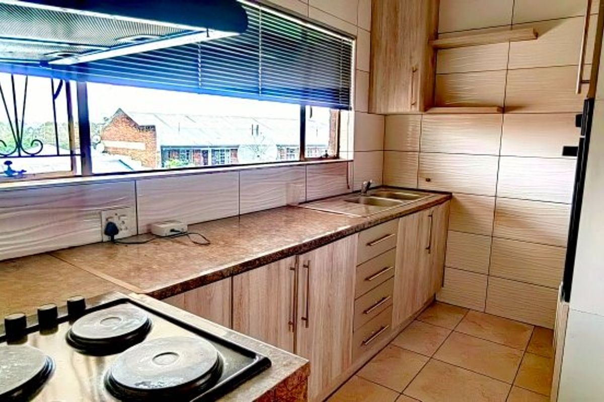 A functional kitchen featuring built-in cabinetry, laminate countertops, an electric hob with extractor fan, and tiled splashbacks.