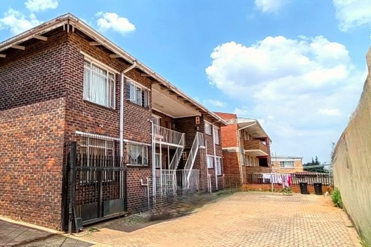 Rear view of a multi-story face brick apartment building featuring external metal staircases and a paved courtyard area.
