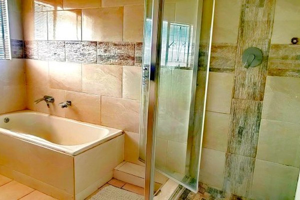 A functional bathroom featuring a built-in bathtub, a separate glass-enclosed shower, and neutral wall tiling throughout.