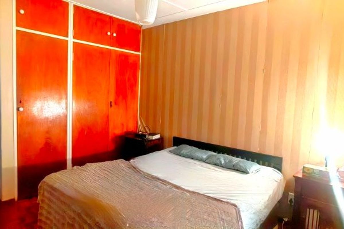 A bedroom featuring built-in cupboards and wooden flooring, currently showing signs of wear and dated interior finishes.