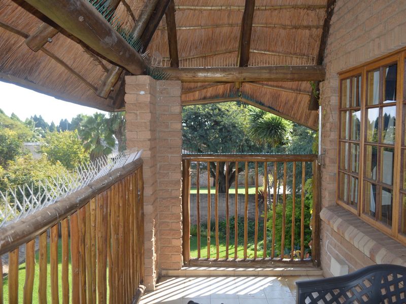 A covered balcony featuring a rustic thatch roof, timber support beams, and a timber balustrade overlooking the garden.