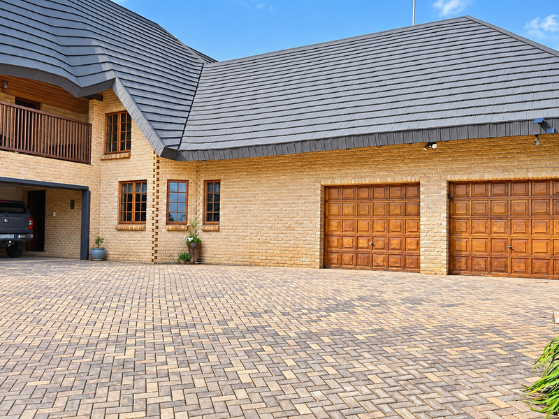 A well-maintained front exterior featuring a double garage with timber doors, a paved driveway, and a balcony overlooking the entrance.
