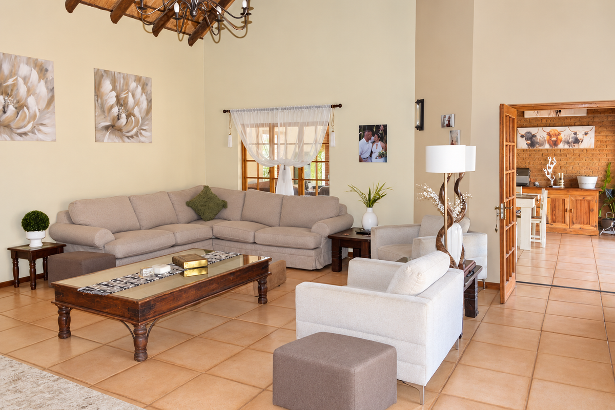 Spacious living room featuring high ceilings with exposed timber beams, ceramic tiled flooring, and double doors leading to an adjacent dining area.