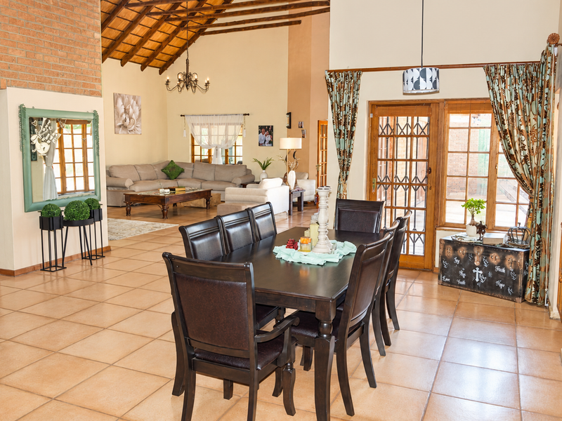 Spacious open-plan living and dining area featuring high vaulted ceilings with exposed timber rafters, ceramic tiled flooring, and direct access to the patio.