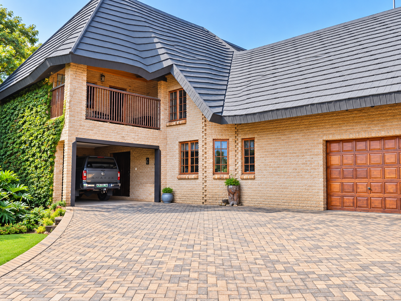 A well-maintained double-story brick home featuring a paved driveway, integrated garage, and an upper-level balcony with timber detailing.
