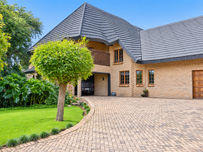 Front elevation of a well-maintained brick house featuring a paved driveway, tiled roof, and integrated garage.