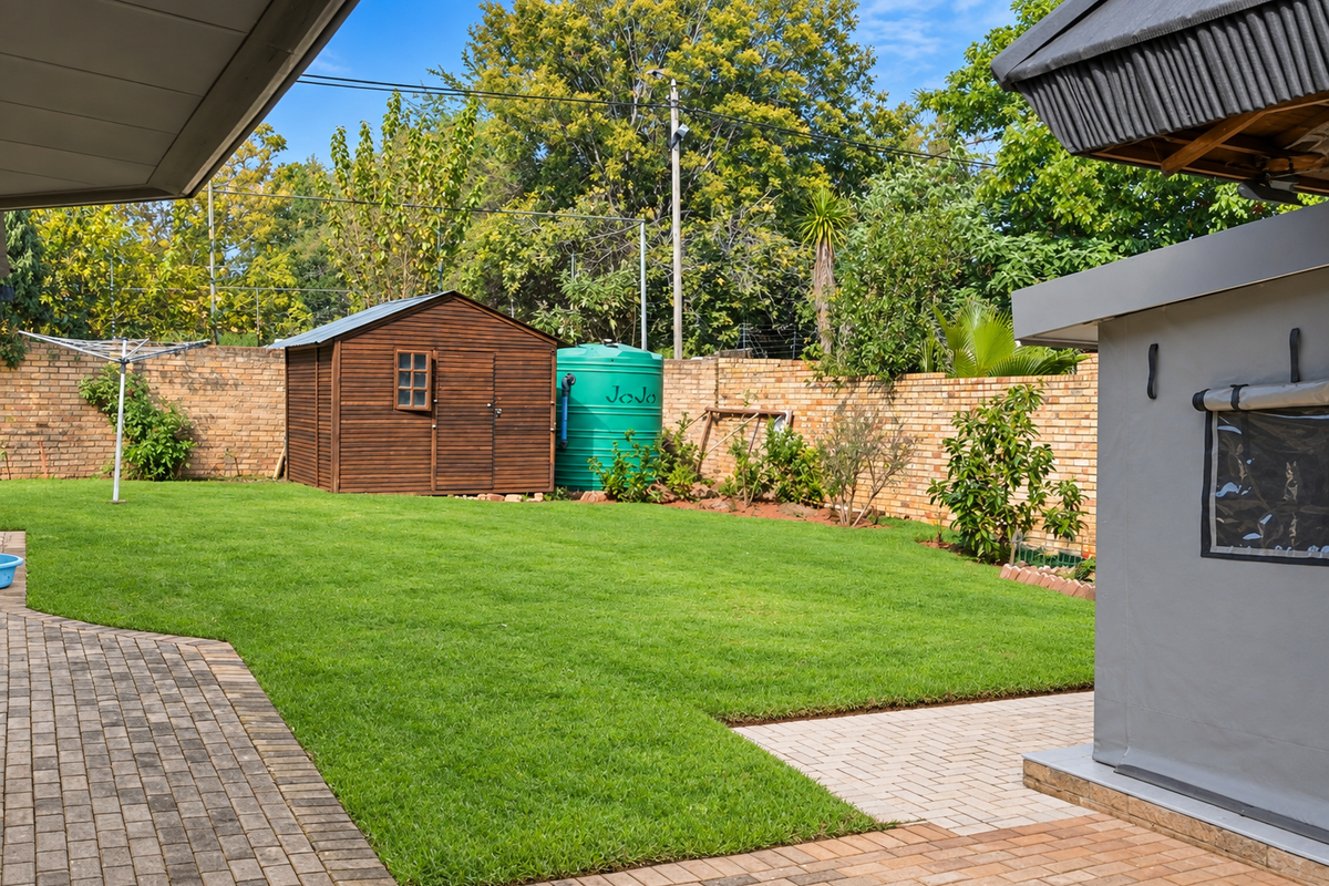 A well-maintained rear garden featuring a paved patio, lush lawn, brick boundary wall, water storage tank, and a wooden garden shed.