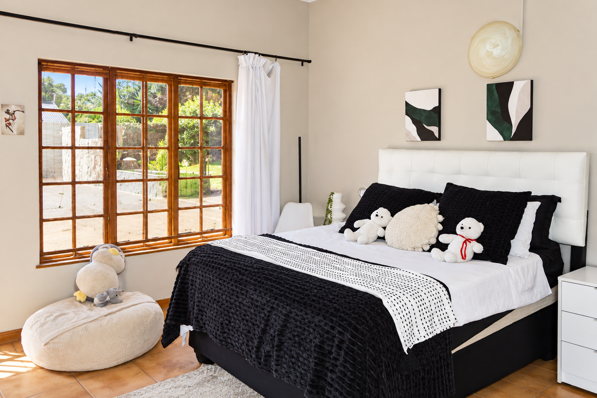 A well-lit bedroom featuring tiled flooring, a large timber-framed window overlooking the garden, and a neutral wall finish.