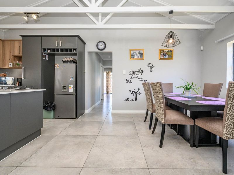 Open-plan kitchen and dining area featuring exposed roof trusses, modern grey cabinetry, a kitchen island, and large format floor tiles.