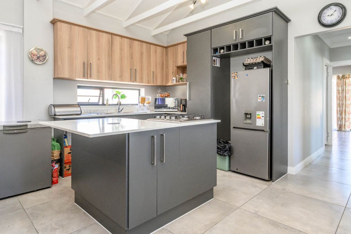 Modern kitchen featuring a central island, two-tone cabinetry, gas hob, and exposed ceiling beams, finished with neutral floor tiles.