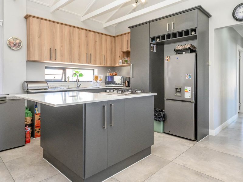 Modern kitchen featuring a central island, two-tone cabinetry, gas hob, and exposed ceiling beams, finished with neutral floor tiles.